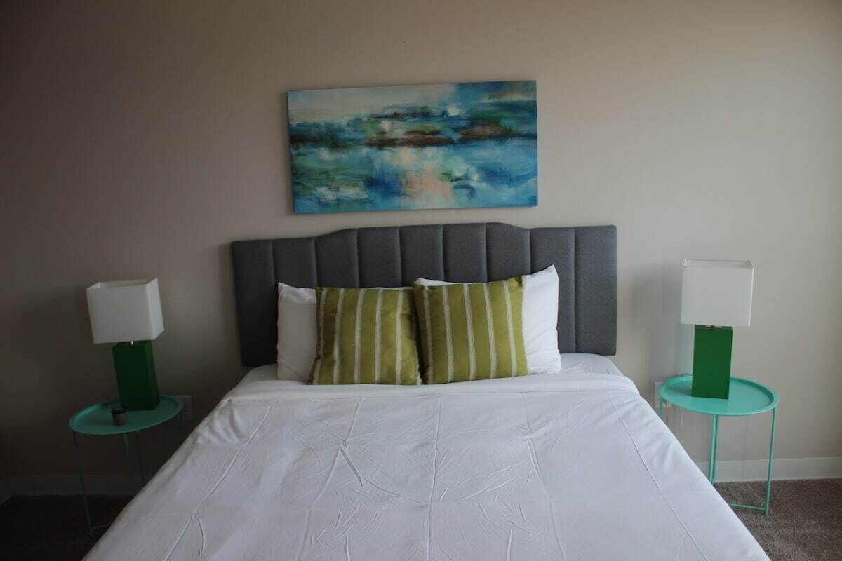 Een hotelkamer met een groot bed, twee nachtkastjes met lampen, een schilderij aan de muur en een kussen met groene strepen.