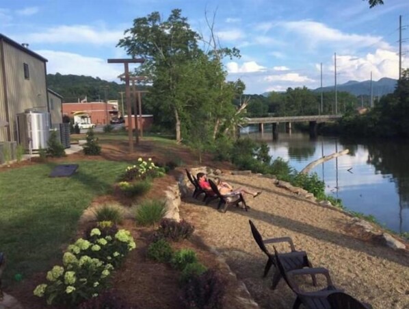 A riverside patio with a person relaxing, a wooden deck, and a view of a bridge and hills. - Cozy & Private 3BR/2BA Country Farmhouse Overlooking Little Tennessee River (Franklin)