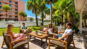 A group of people seated on wicker furniture outdoors with a white fence and palm trees in the background. - Miami & Me Oasis: Dive into Beach Bliss, King Size Comfort, and Gulfside Glam! (Indian Rocks Beach)
