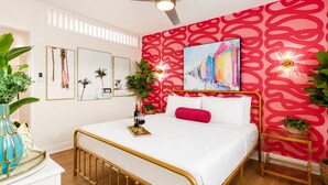 A bedroom with a bed, a ceiling fan, a red patterned wall, and framed artwork. - Miami & Me Oasis: Dive into Beach Bliss, King Size Comfort, and Gulfside Glam! (Indian Rocks Beach)