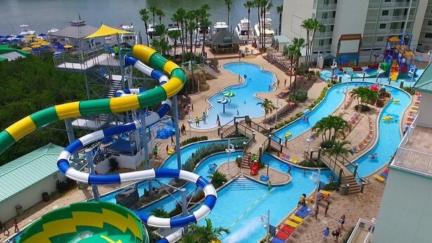 A water park with multiple pools and slides, surrounded by palm trees and a building with balconies. - Miami & Me Oasis: Dive into Beach Bliss, King Size Comfort, and Gulfside Glam! (Indian Rocks Beach)