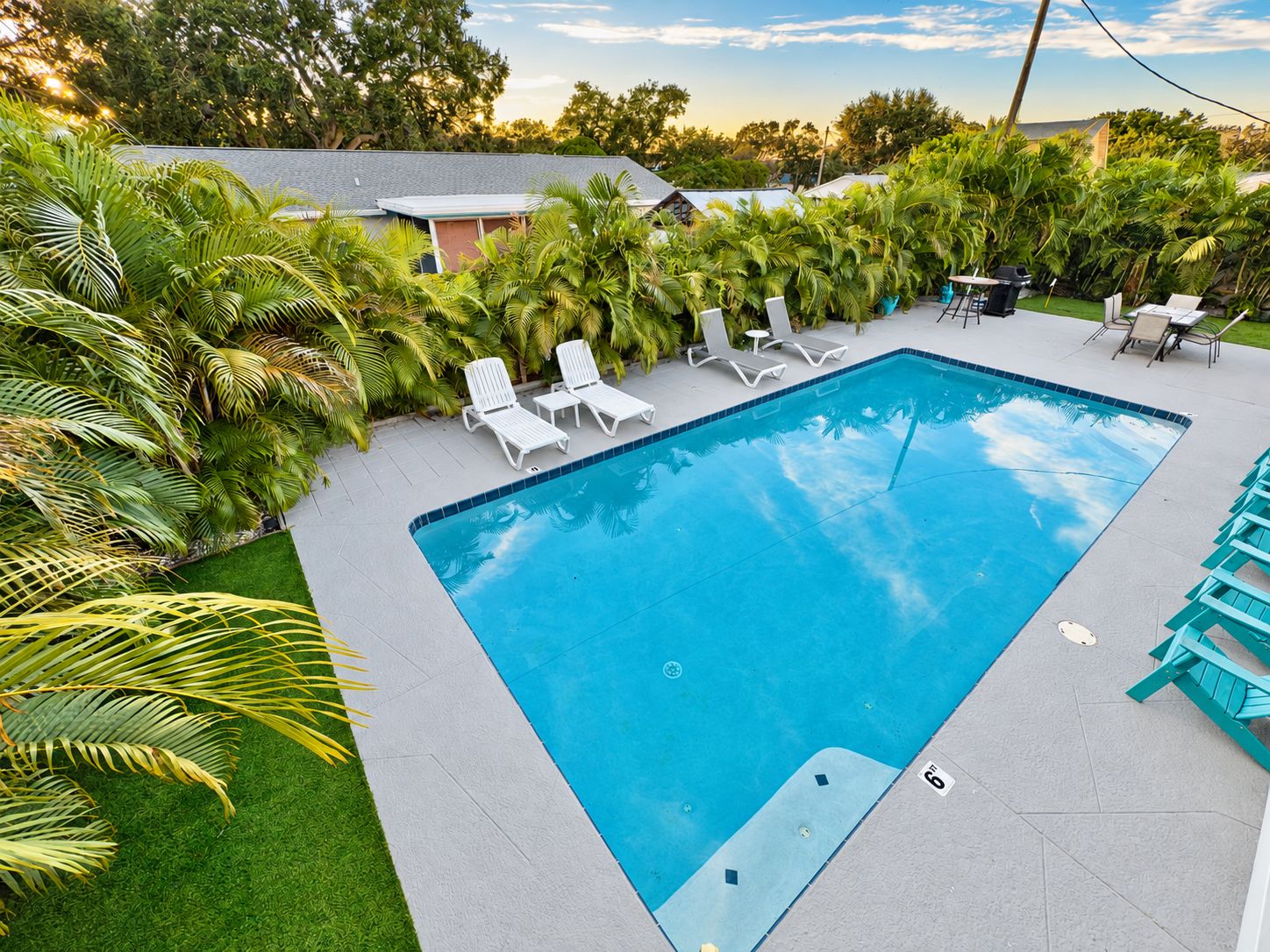 Una piscina rectangular con borde de azulejos, rodeada por un patio con sillones blancos y una pequeña mesa.