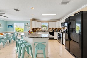Una cocina moderna con una isla central, electrodomésticos de acero inoxidable y sillas color turquesa.