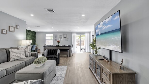 Een moderne woonkamer met een grijze bank, een salontafel met een plant, een televisie aan de muur en uitzicht op de oceaan door een schuifdeur.