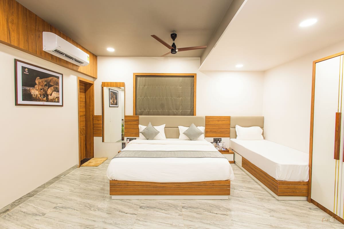 Ein Hotelzimmer mit einem großen Bett, einem kleineren Bett, einem Deckenventilator, einer Klimaanlage und einem gerahmten Bild an der Wand.