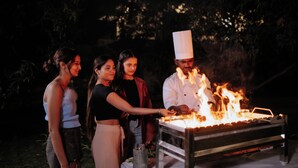Uno chef cucina all'aperto su una griglia da campeggio, circondato da tre persone.