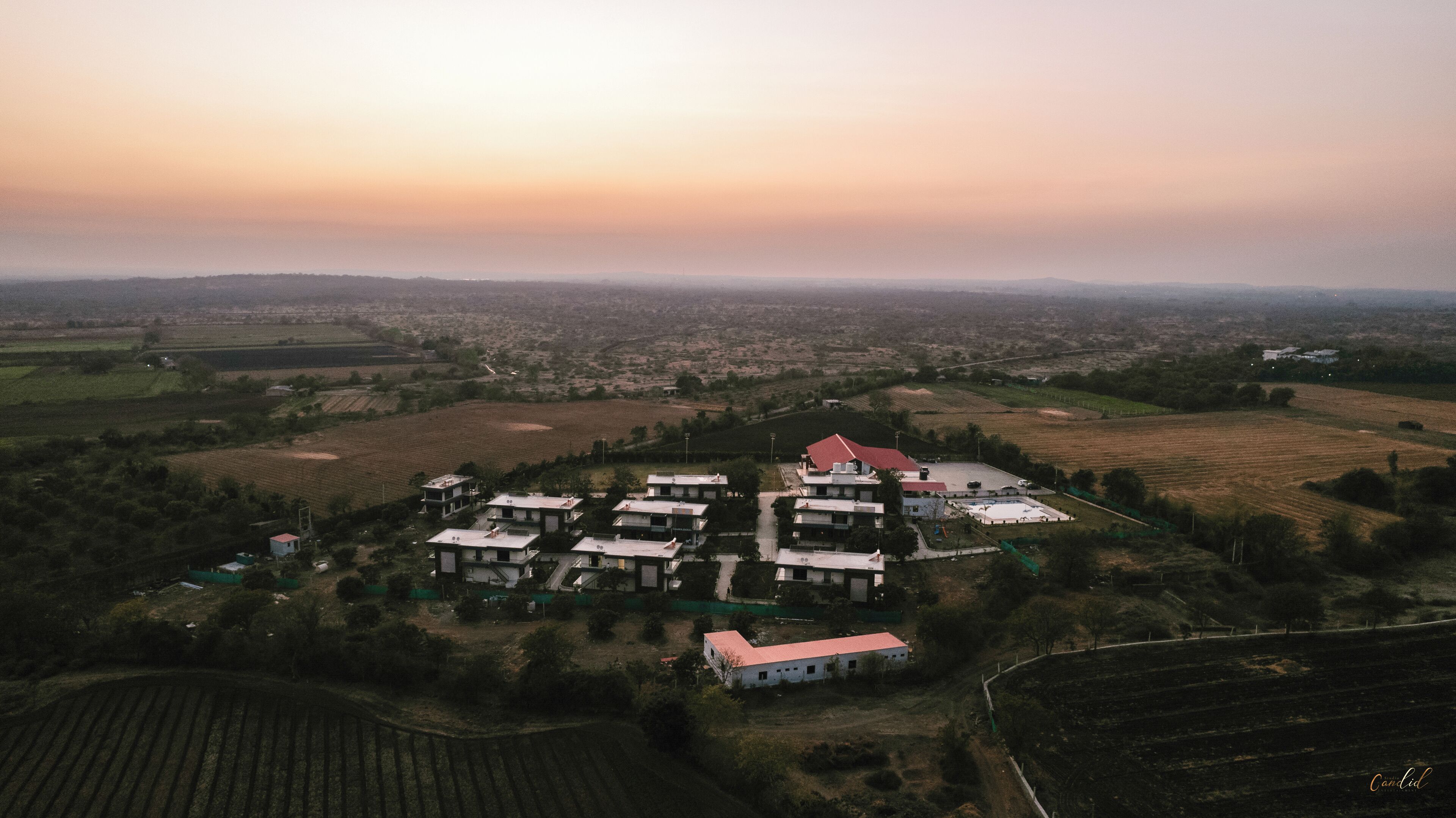 Vista aérea de una zona residencial con varios edificios, incluyendo una casa grande con techo rojo y varias construcciones más pequeñas.