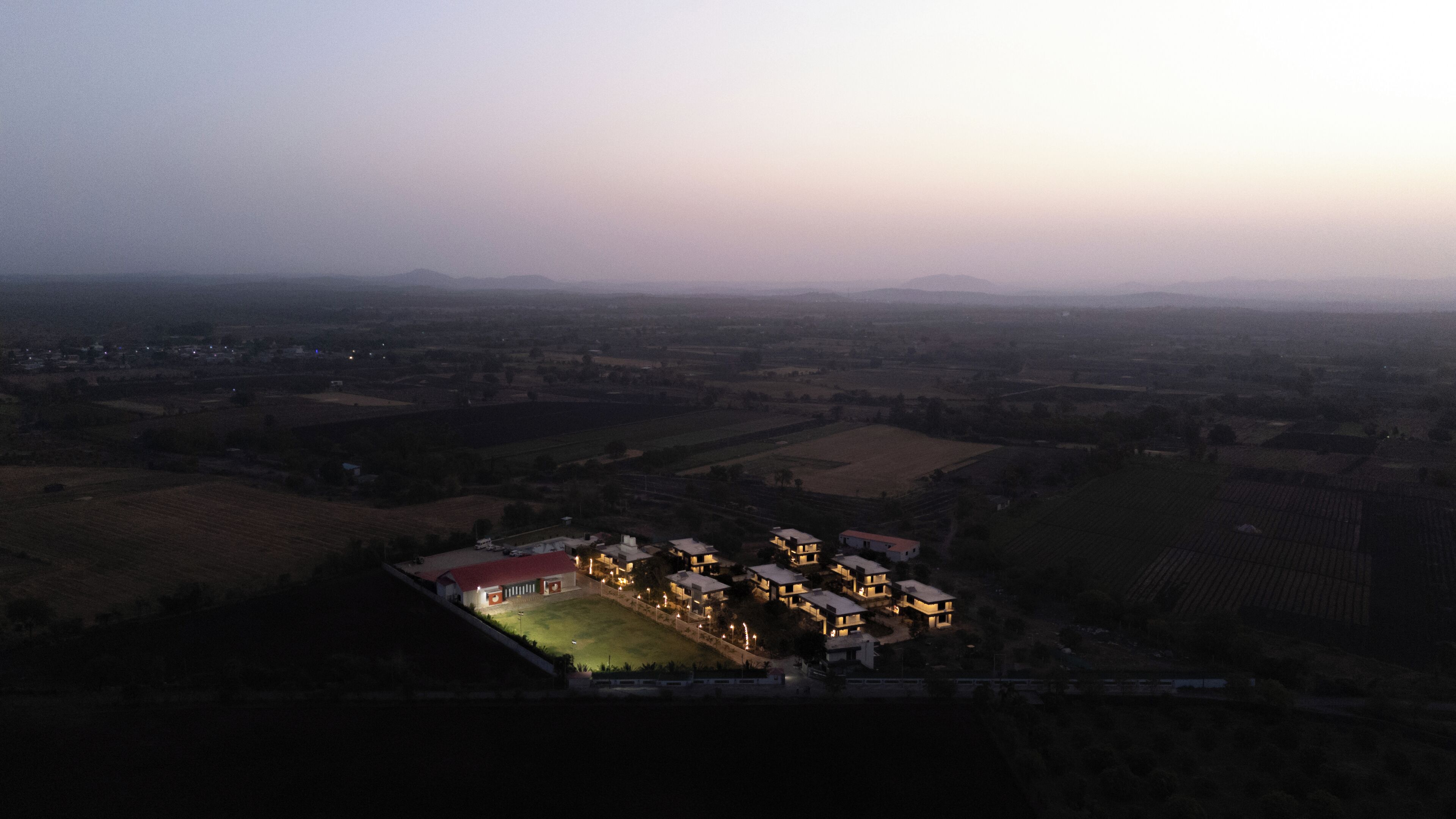 An aerial view of a residential area with multiple houses, a large open field, and distant mountains.