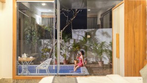 Una donna seduta vicino a una porta di vetro, con vista su una zona piscina con piante in vaso e un tavolo da pranzo.