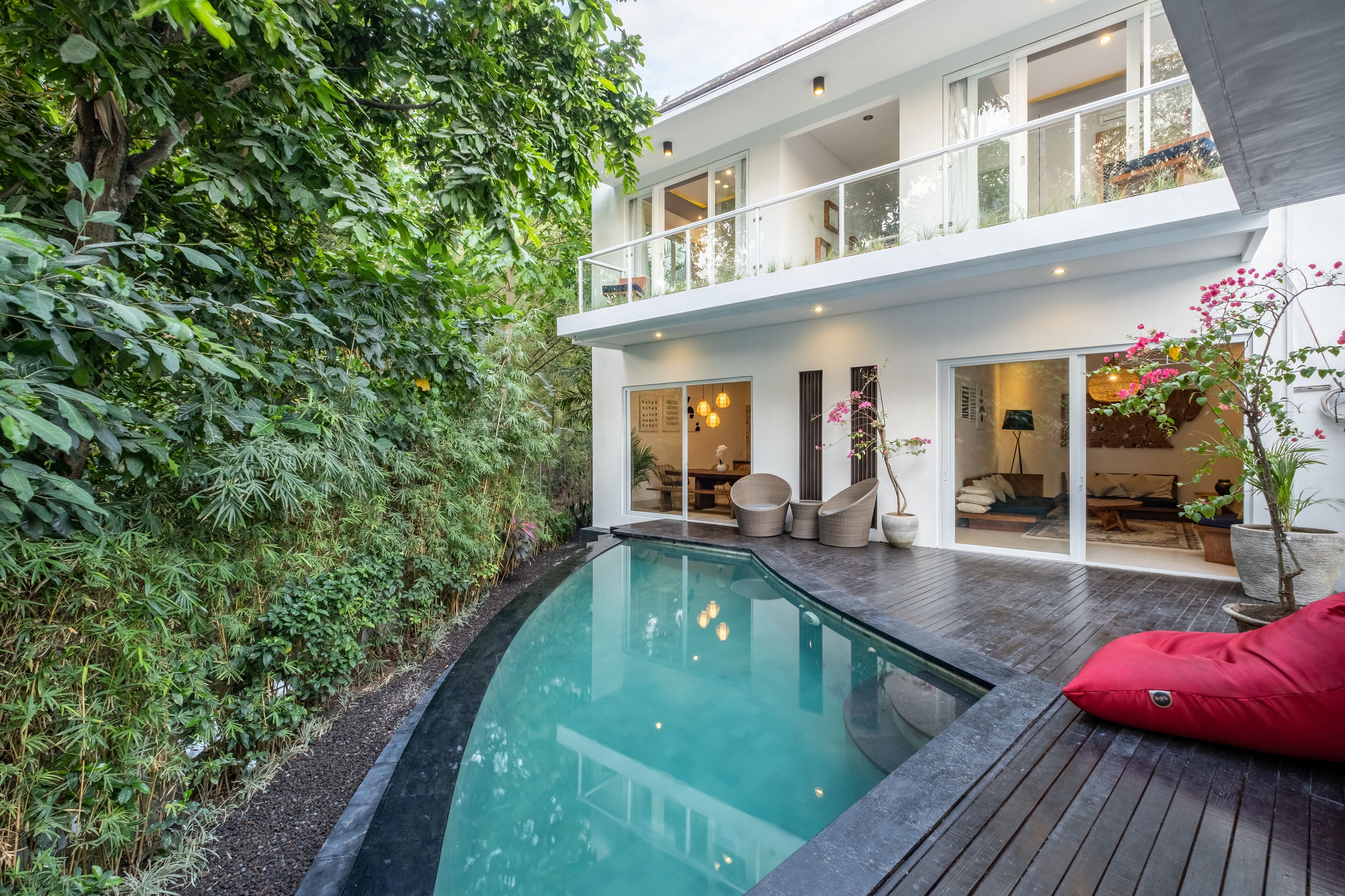 A modern house with a swimming pool, a balcony, and lush greenery.