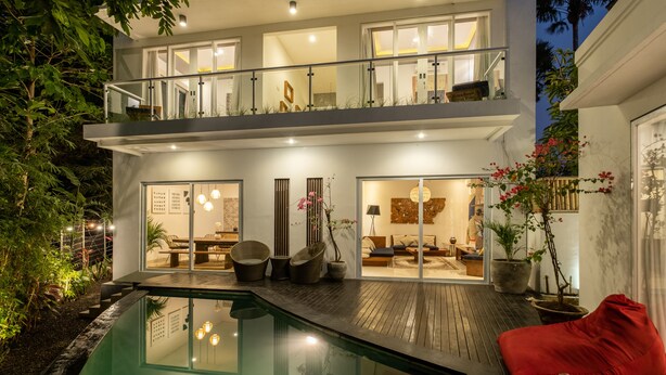 Une maison moderne à deux étages, dotée d’un balcon en verre, d’une piscine et d’un intérieur bien éclairé.