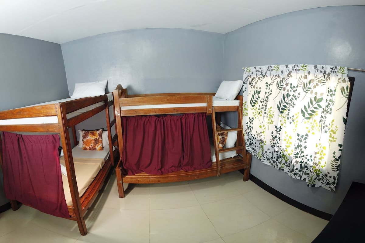 A room with two wooden bunk beds, a small shelf, and a curtain with a leaf pattern.