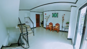 Amplia sala de estar con escalera, dos sillones de madera con cojines estampados, un cuadro enmarcado en la pared y una planta en maceta.