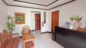 Un área de recepción con un mostrador de madera, una silla, una mesita y un cuadro en la pared.