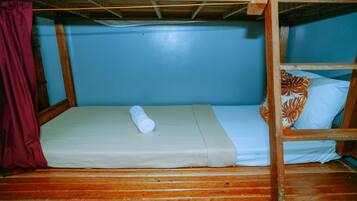 A bunk bed with a rolled towel on the lower bunk, a pillow with a leaf pattern, and a maroon curtain.
