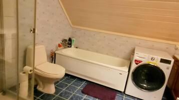 Een kleine badkamer met toilet, een bankje, een wasmachine en een douchecabine met glazen wanden.