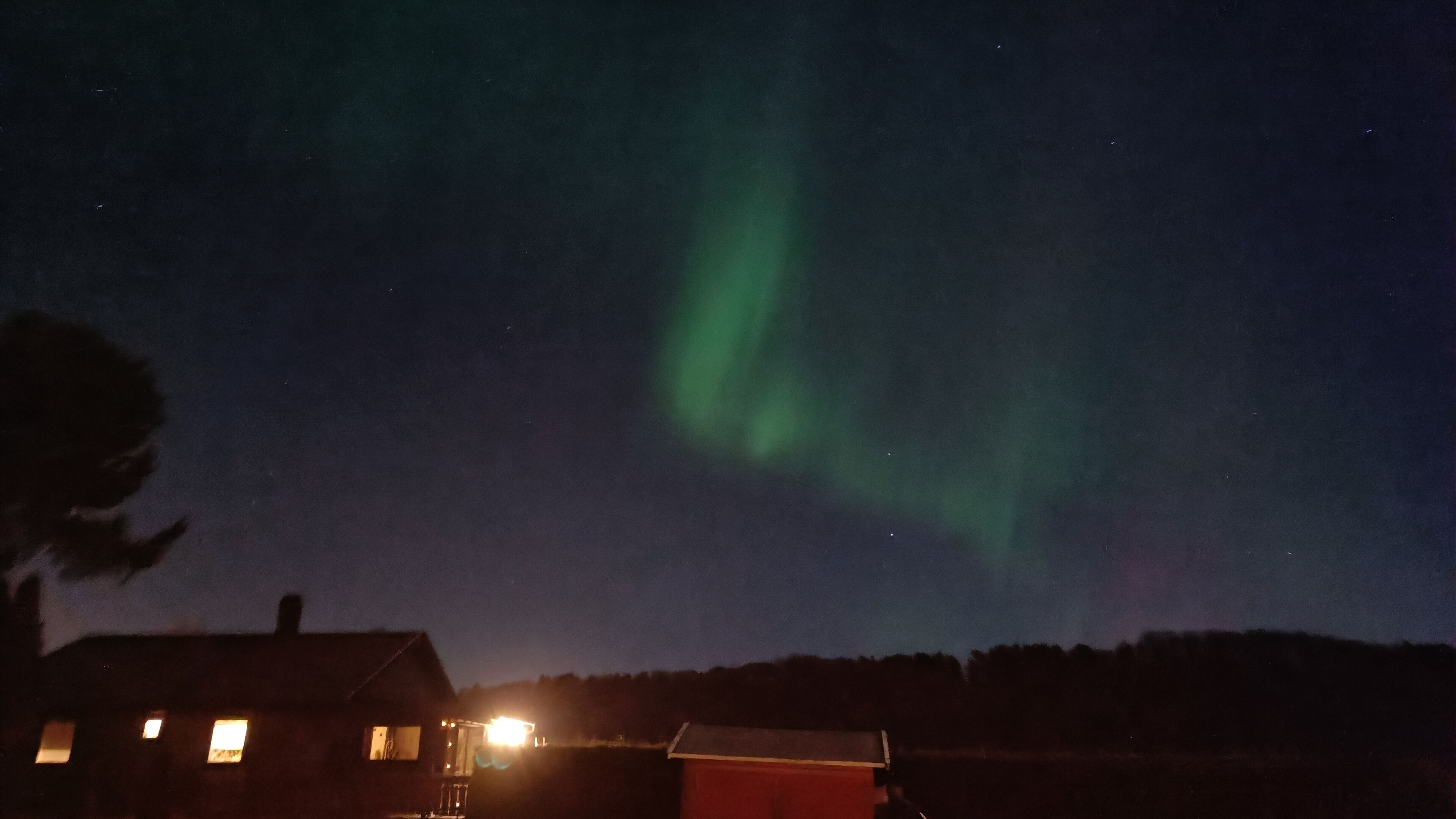 A house with a visible window and a small attached structure, possibly a shed, under a night sky with the aurora borealis.