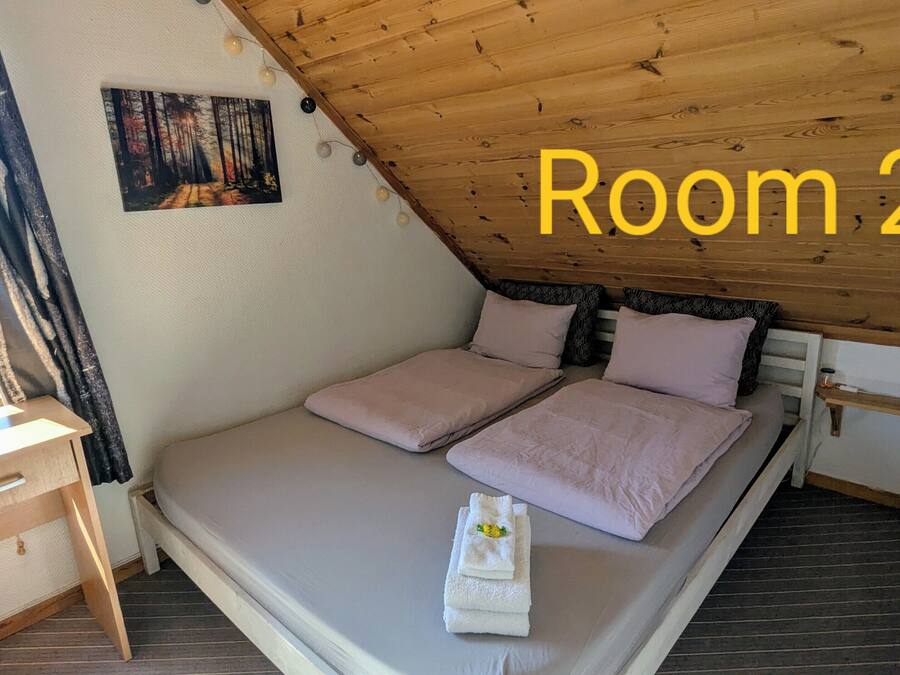 Un dormitorio con cama, almohadas, una mesita de noche, un cuadro y vistas al exterior.
