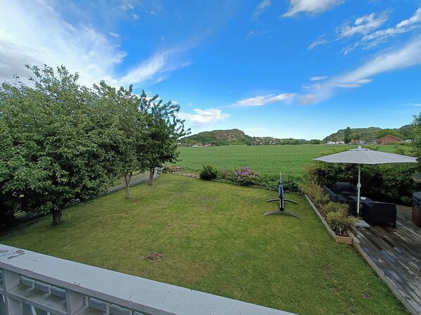 A backyard with a grassy lawn, a tree, a patio with outdoor furniture, and a view of a distant hill. - Mikael's Bed & Spa (Sandefjord)