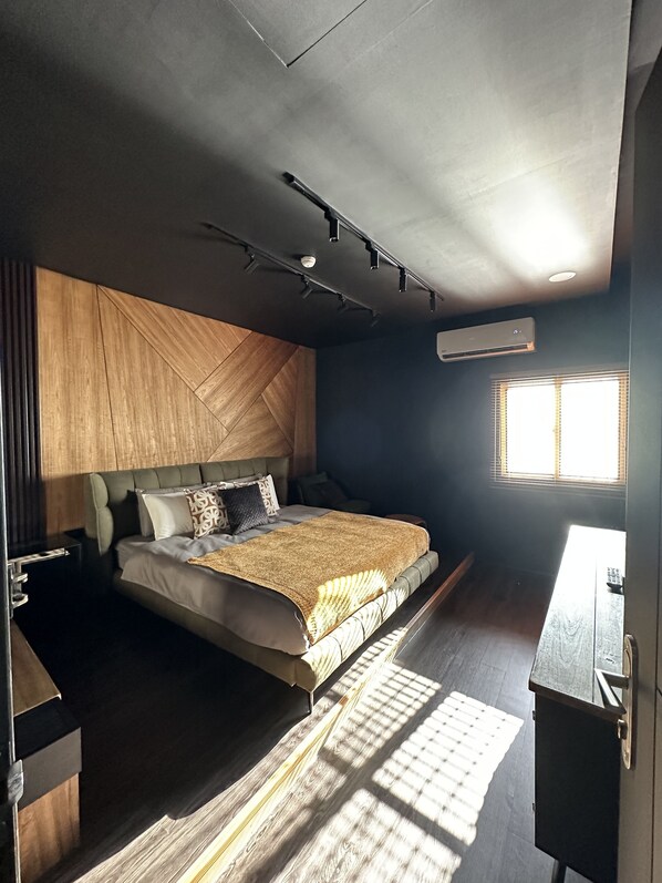 Un dormitorio moderno con cama, mesitas de noche, aire acondicionado y una ventana con persianas.