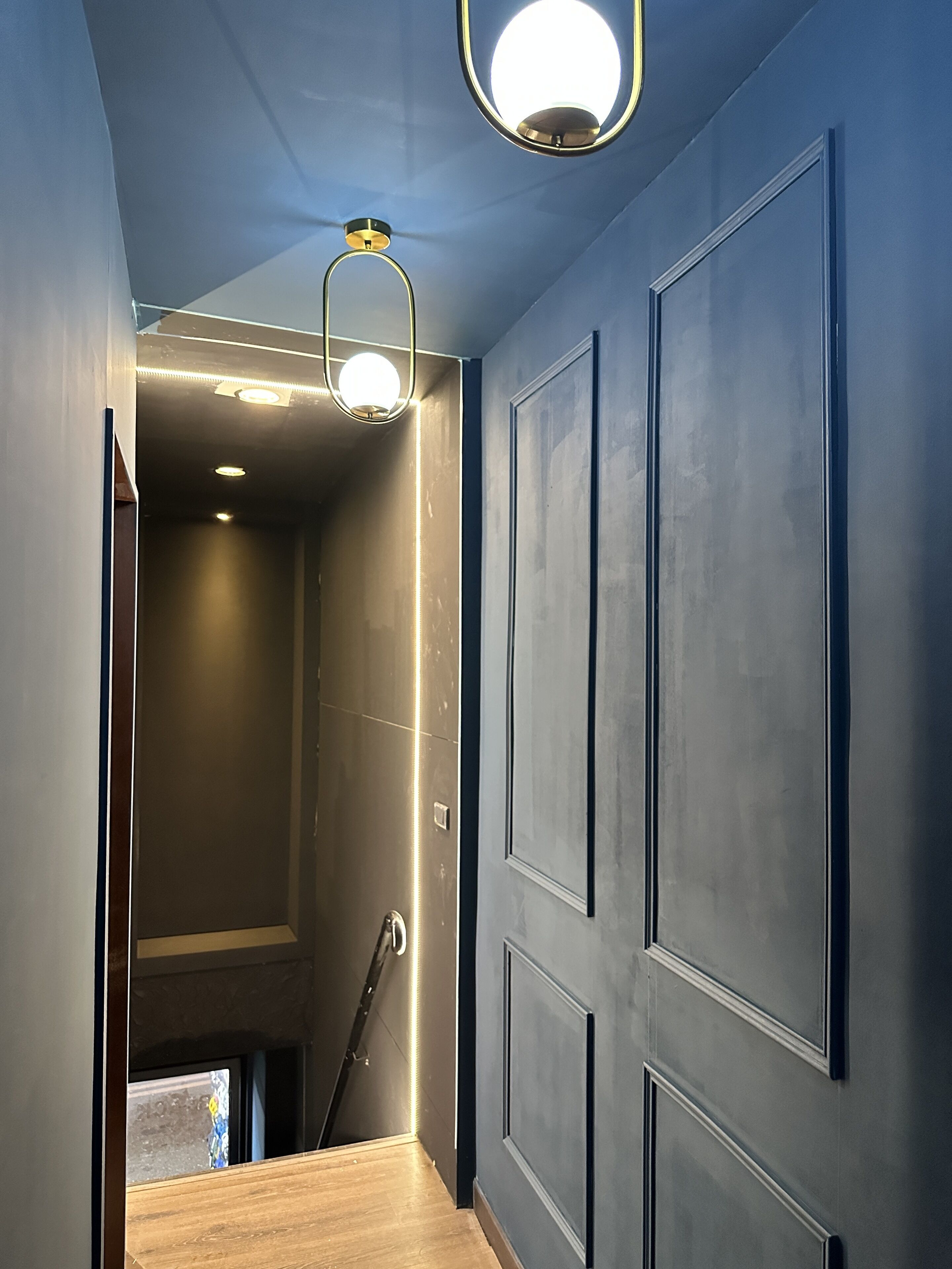 A hallway with dark blue walls, a wooden floor, and a staircase leading to another level.