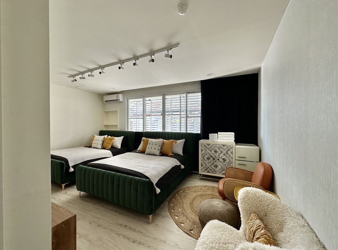 A modern bedroom with two beds, a dresser, and a window.