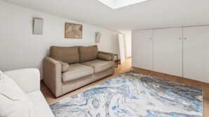 A modern living room with a high ceiling skylight, a beige sofa, a patterned rug, and a white wardrobe.