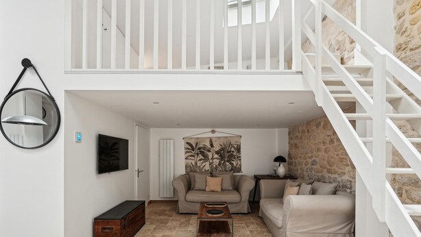 A spacious living area with a high ceiling, a staircase, and a stone wall.