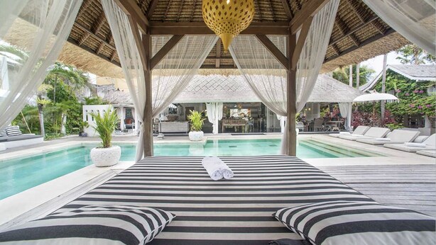A bed with striped bedding and a canopy, a pool, and outdoor seating with umbrellas.
