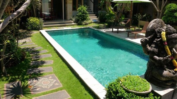Una piscina con una estatua de piedra, rodeada de abundante vegetación y un césped cuidado.
