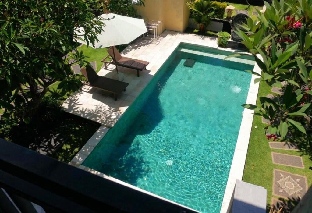 A rectangular swimming pool with clear water, surrounded by a patio area with lounge chairs and an umbrella.