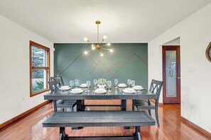 Comedor con una mesa de madera oscura dispuesta para seis comensales, una lámpara moderna y una pared de acento verde.
