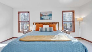 Un dormitorio con una cama, dos mesitas de noche, una lámpara de pie y un cuadro en la pared.