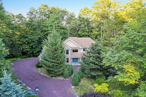 A house surrounded by dense forest with a driveway leading to a front door.