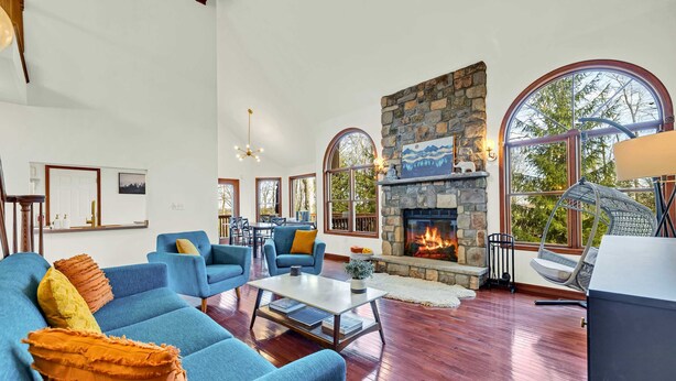 Ein geräumiges Wohnzimmer mit blauen Sofas, einem Steinkamin, großen Bogenfenstern und einem Essbereich.