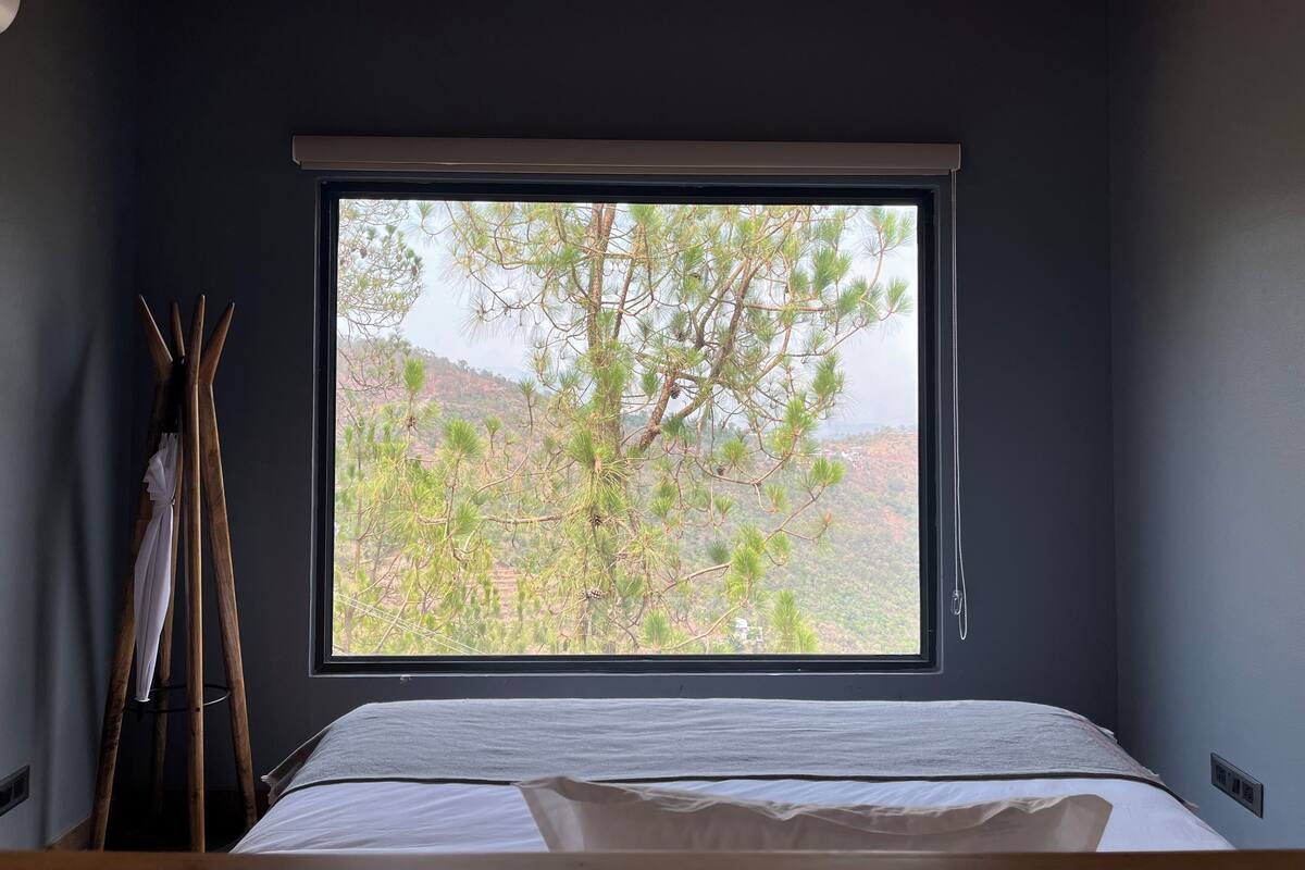 Un dormitorio con un ventanal grande, una cama y una escalera de madera apoyada en la pared.