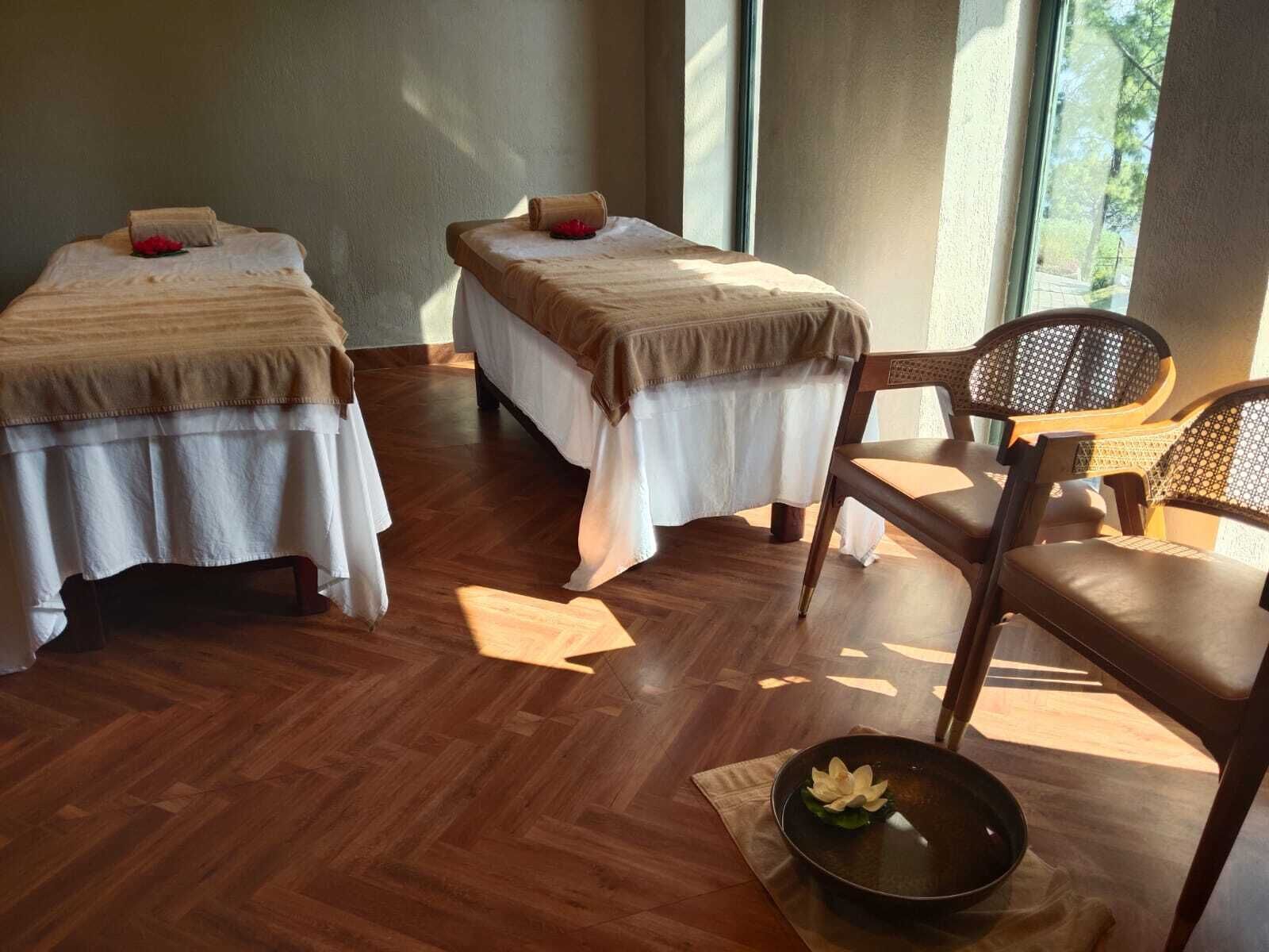 Une chambre avec deux lits, un plancher en bois et une chaise sur laquelle est posé un vase de fleurs.