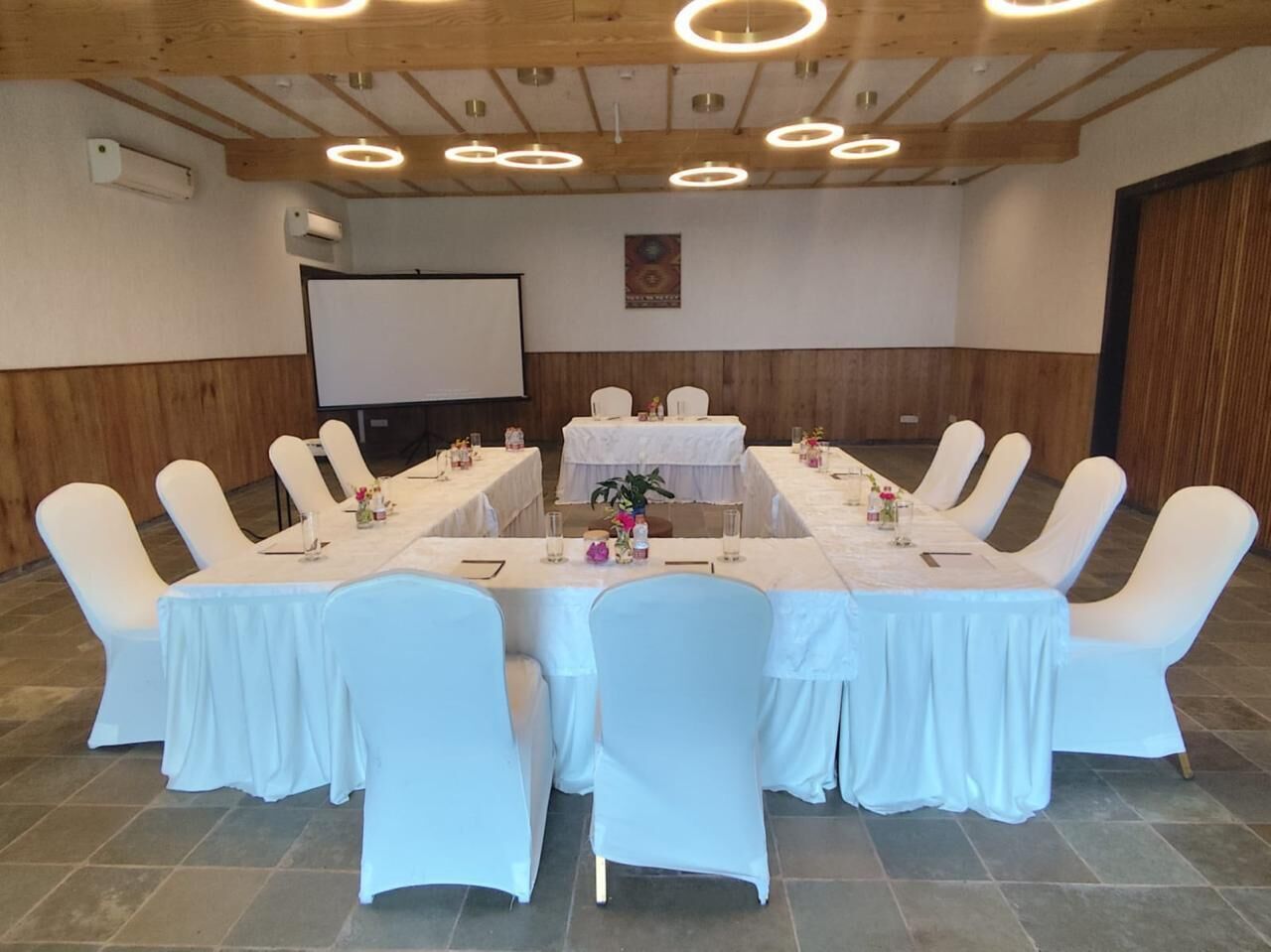 A conference room with a long table, white chairs, and a projector screen.