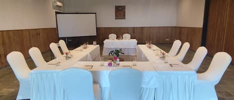 A conference room with a long table, white chairs, and a projector screen.
