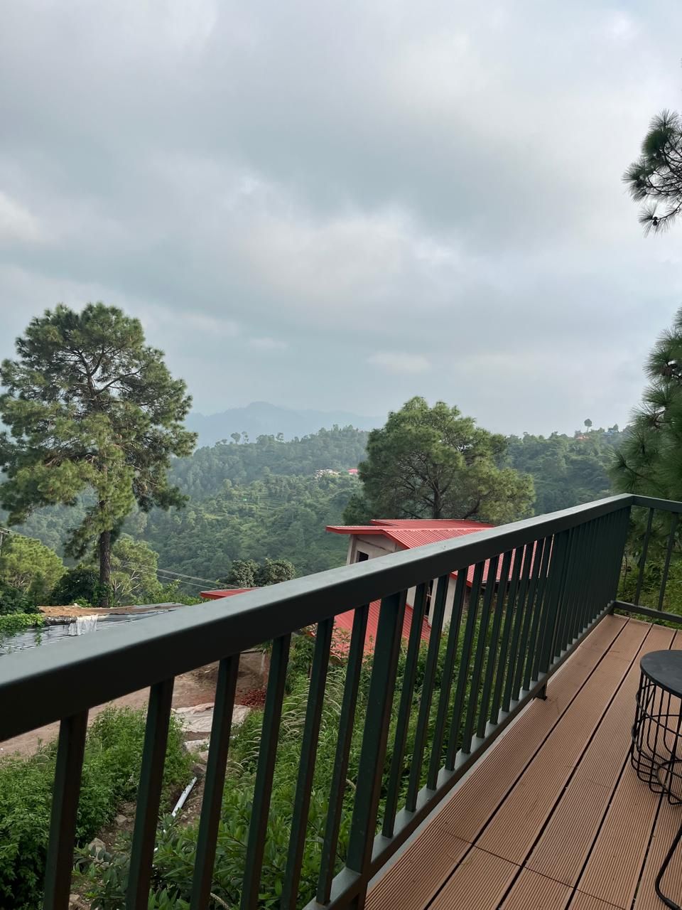A balcony with a view of a mountainous landscape, a red-roofed building, and a wooden deck.