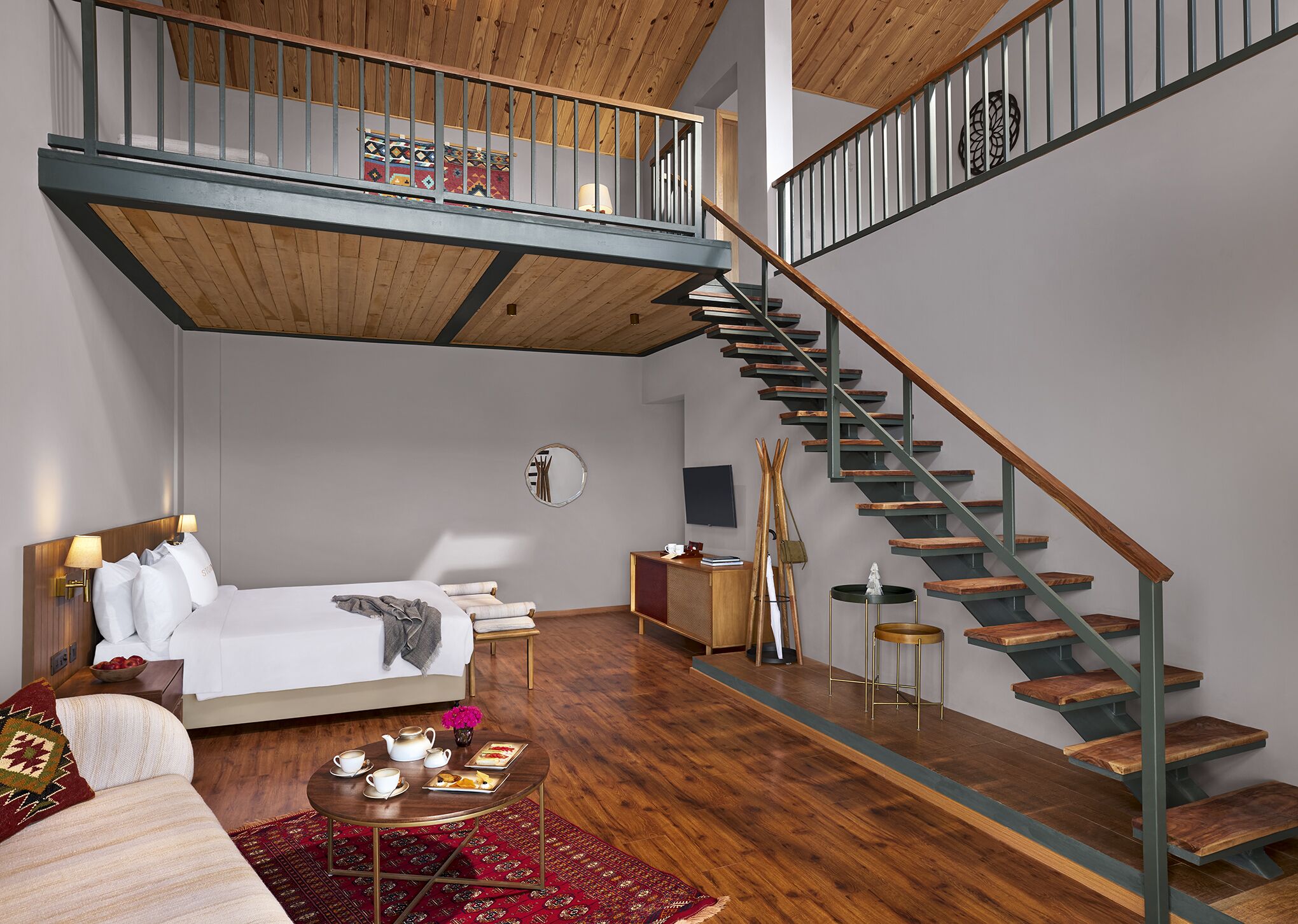 Un dormitorio moderno con un entrepiso para dormir, una escalera de madera y una zona de comedor con una mesa de centro.