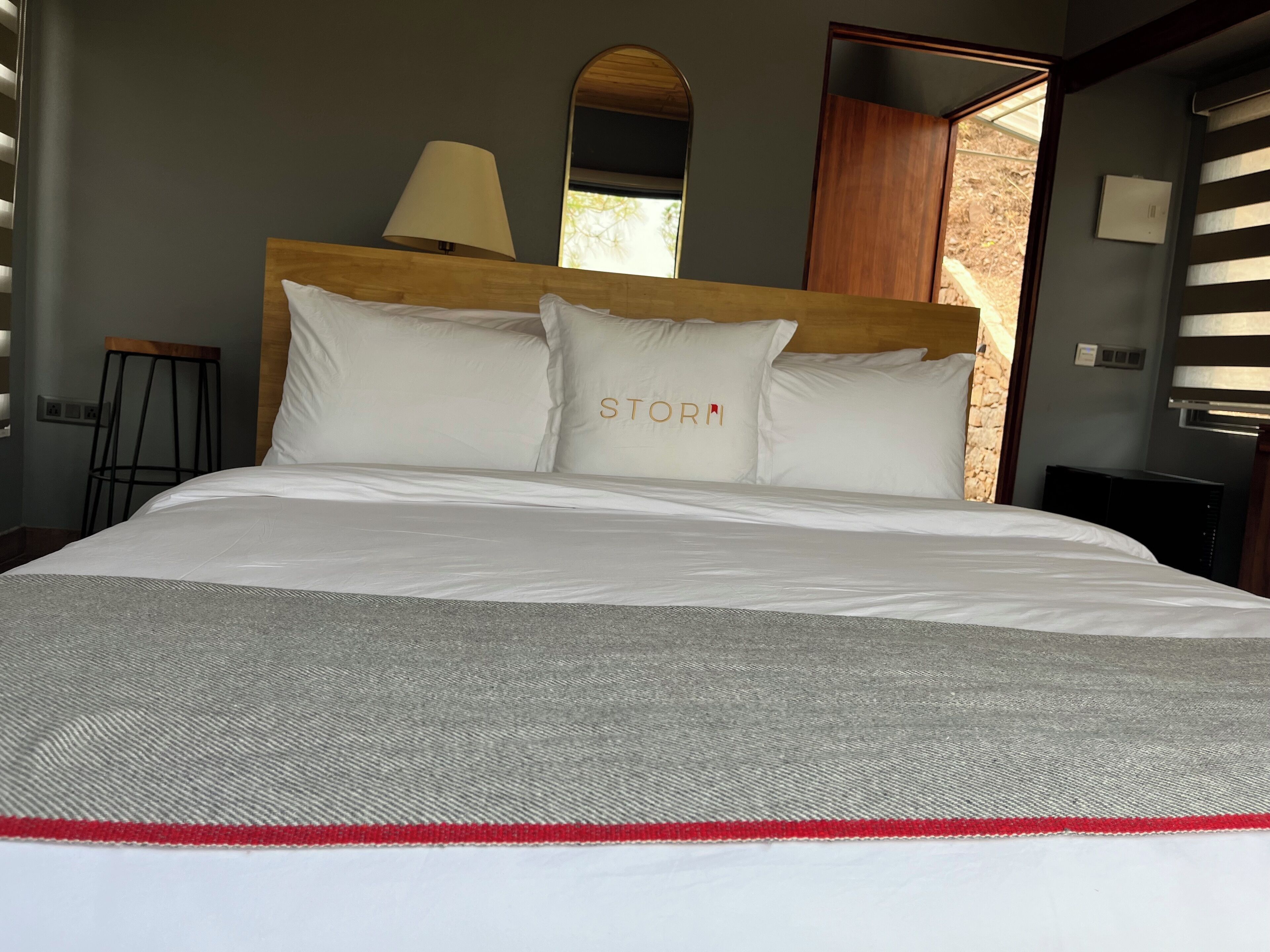 A bed with white bedding and a grey and red striped area at the foot.