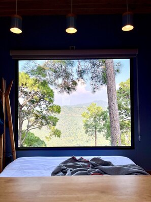 A bedroom with a large window, a bed with a gray blanket, and wooden furniture. - Storii by ITC Hotels The Kaba Retreat (Solan)