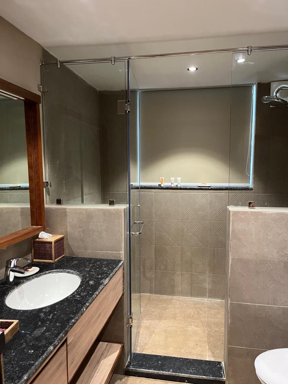 Un baño moderno con ducha envuelta en vidrio, un espejo grande y encimera de granito con lavamanos.