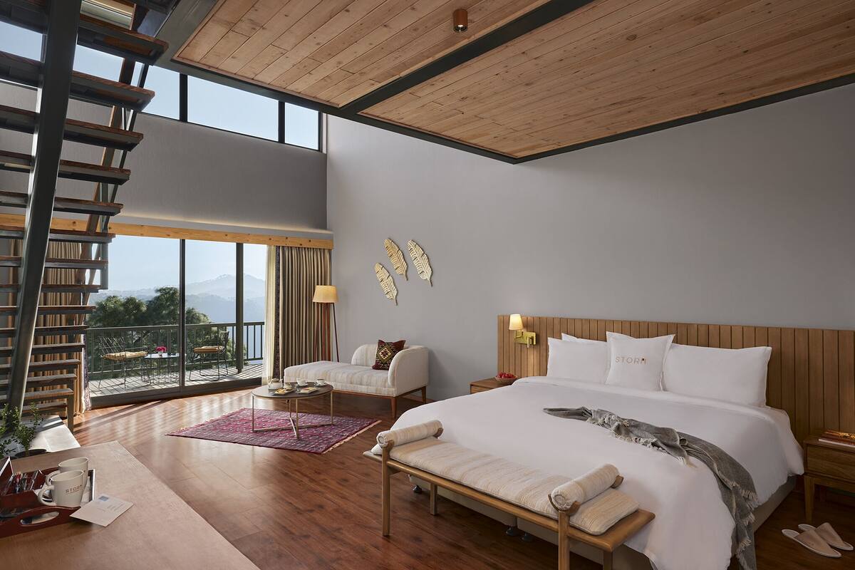 Un dormitorio espacioso con una cama grande, cabecera de madera, balcón con vistas y una escalera.