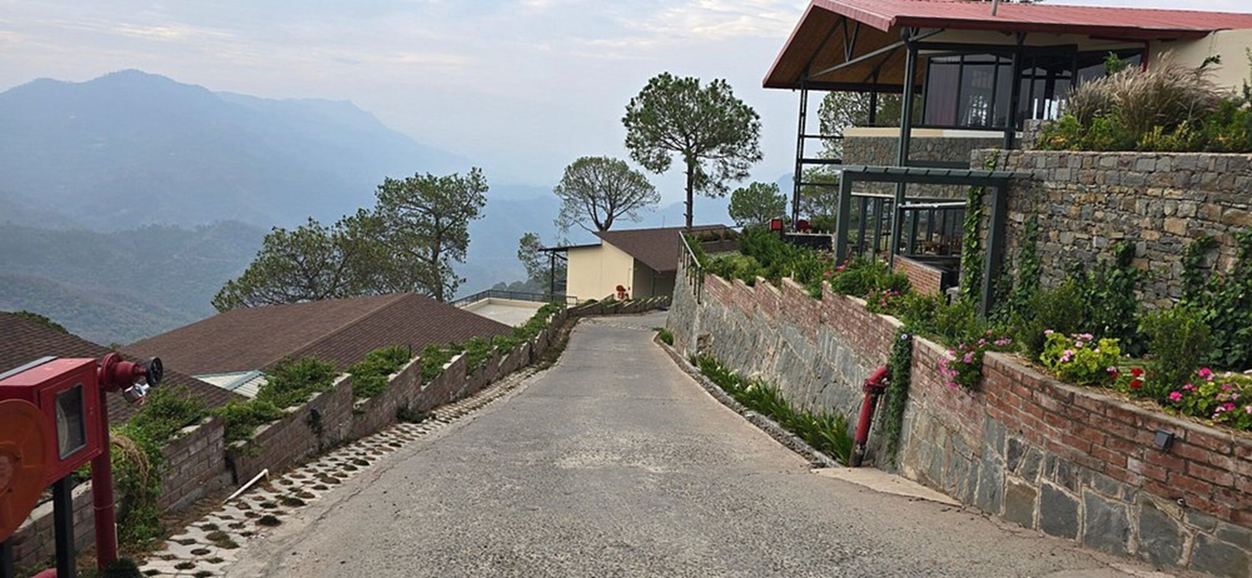 Une route étroite et pavée, bordée de bâtiments aux murs de pierre et aux fondations en briques, qui mène vers une chaîne de montagnes.