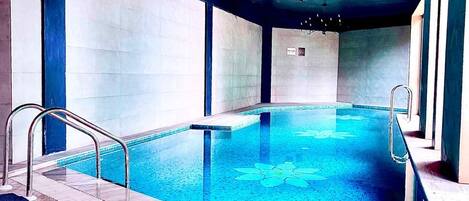 Una piscina interior con diseño de suelo azul, barandillas metálicas y un techo con luminarias visibles.