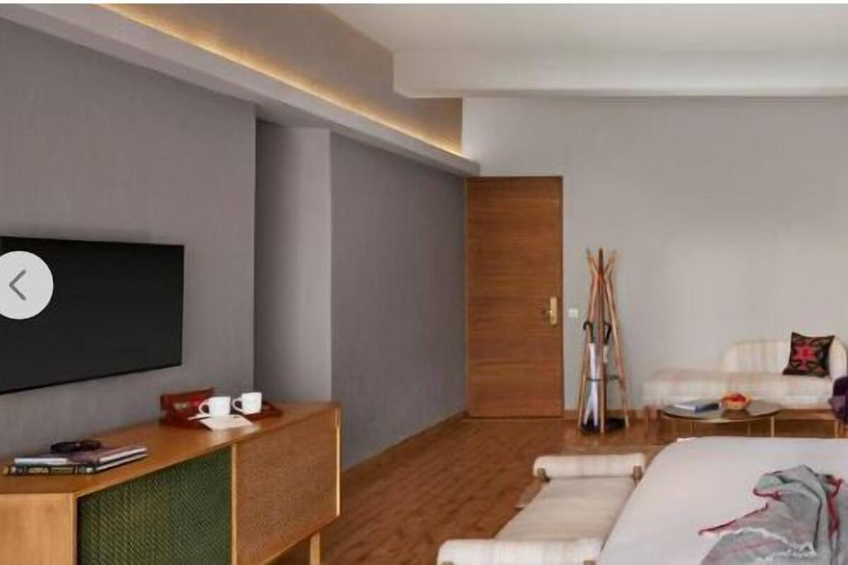 Una habitación de hotel moderna con una cama grande, un televisor de pantalla plana, un cabecero de madera y un pequeño escritorio con lámpara.