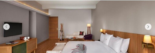 A modern hotel room with a large bed, a flat-screen TV, a wooden headboard, and a small desk with a lamp. - Storii by ITC Hotels The Kaba Retreat (Solan)