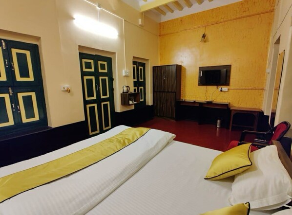 A hotel room with a bed, a desk, a television, and a wardrobe. - Tulin Heritage Bungalow (Purulia)